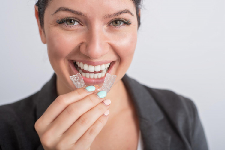 an woman is holding an adult Invisalign in front of her teeth. 