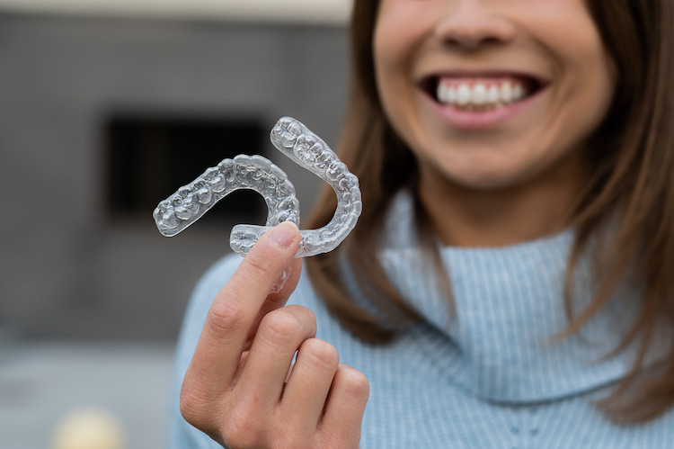 a smiling woman holding a pair of Invisalign with her hand.