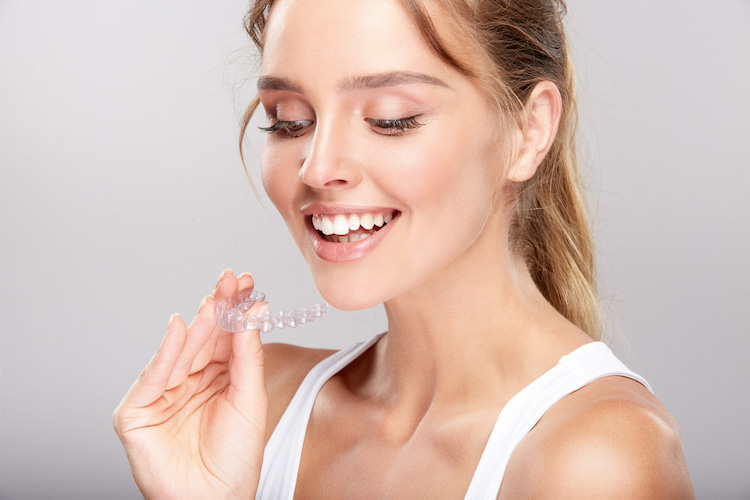 a smiling woman holding an Invisalign